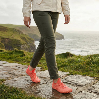 Coral orange walking shoes worn on a coastal path, side view