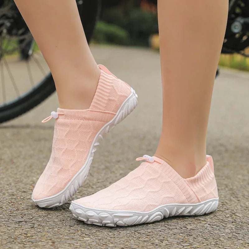 Pink barefoot-style shoes worn outdoors, side view