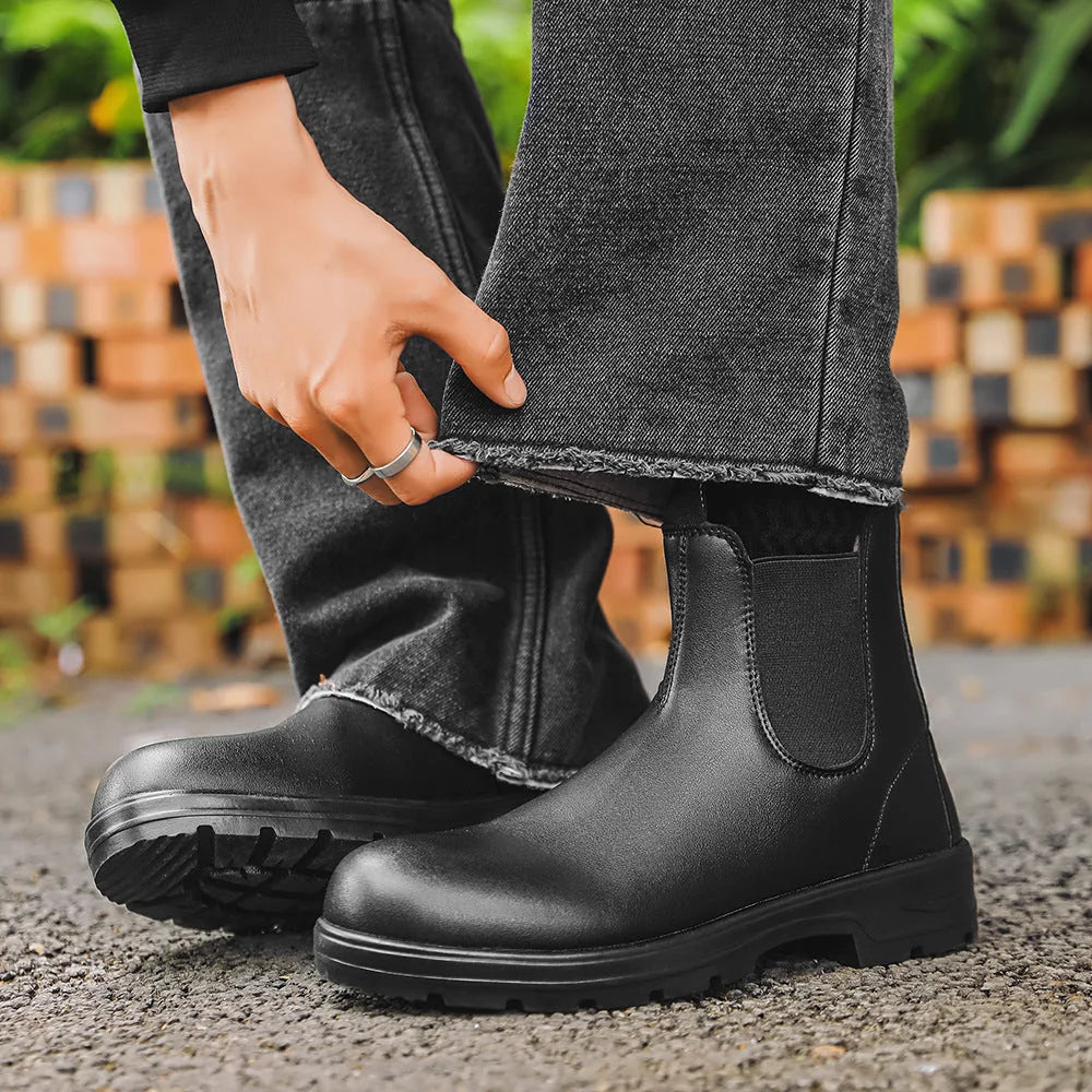 Black Chelsea boots held beside dark jeans, front view
