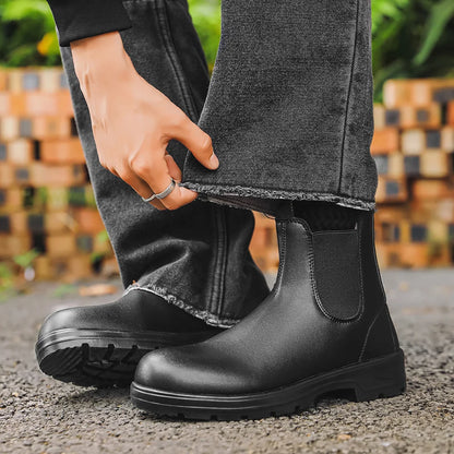 Black Chelsea boots held beside dark jeans, front view