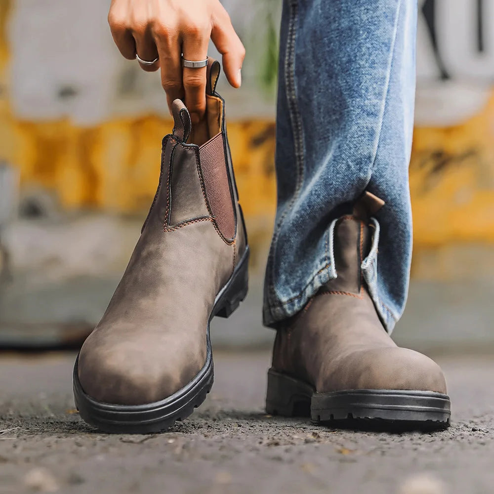 Brown Chelsea boots carried beside dark jeans, side view