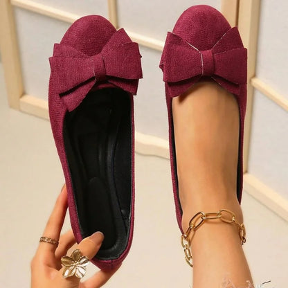 Women's burgundy bow ballet flats shown on foot with one shoe held